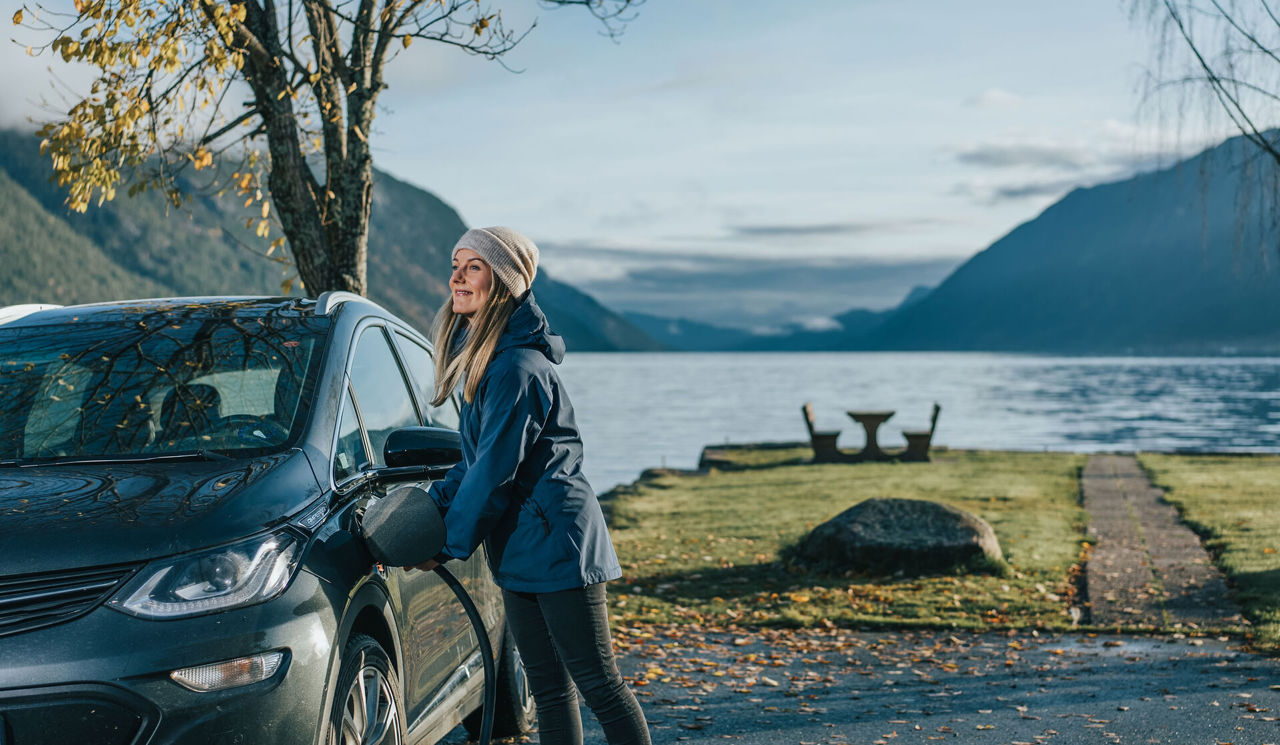 Dame lader bilen ved en ladestasjon