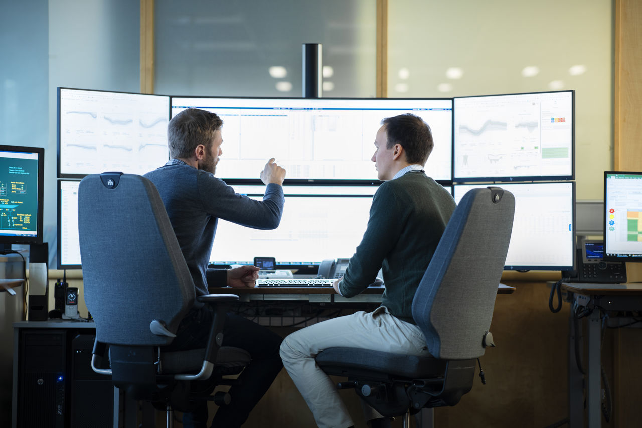 To menn ser på store skjermer i et kontorlandskap 