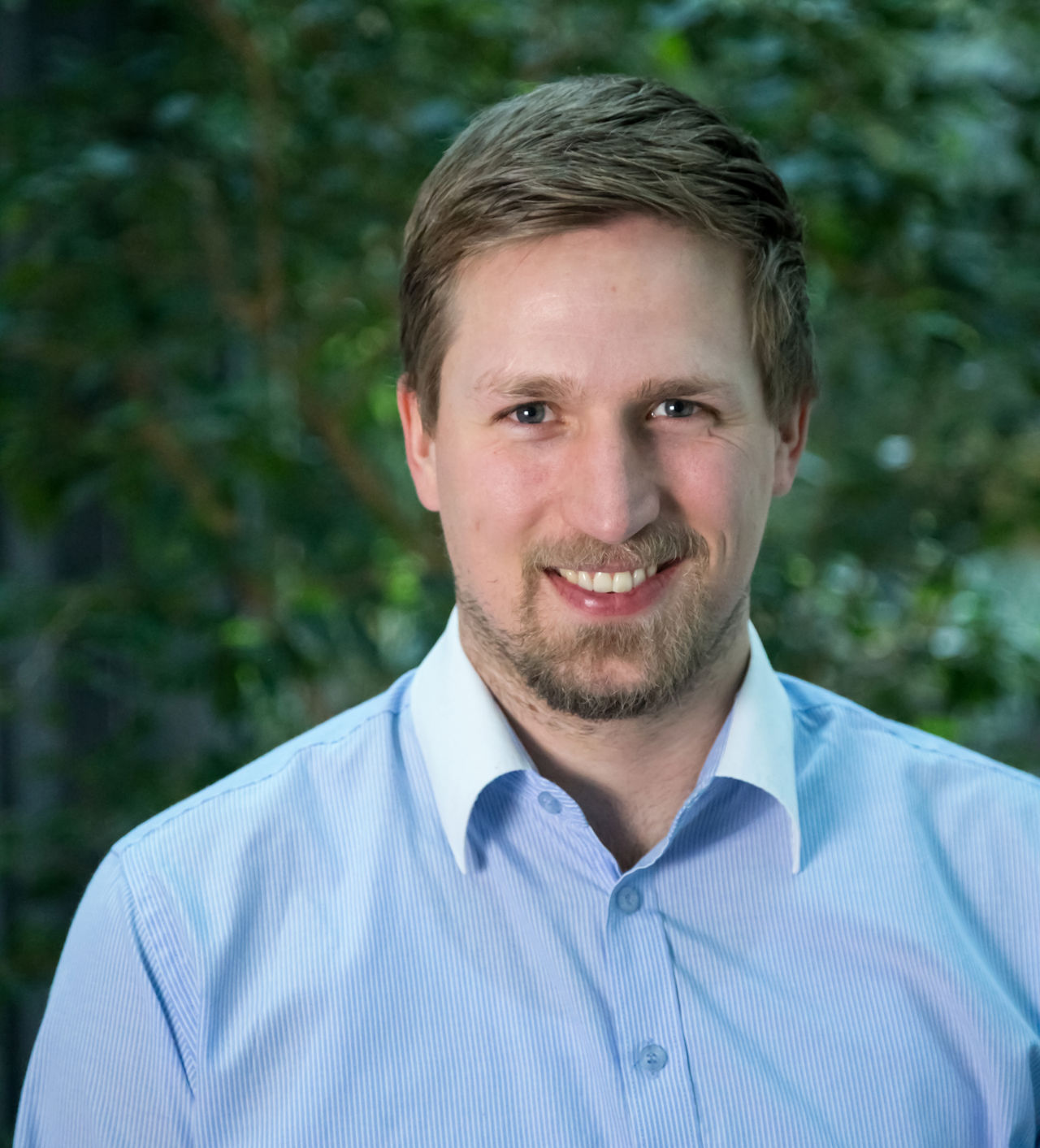 Mann i bl&aring; skjorte smiler til kameraet