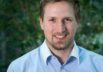 Mann i blå skjorte smiler til kameraet