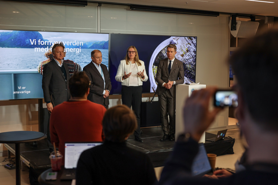 Fire personer står på et podium under en pressekonferanse