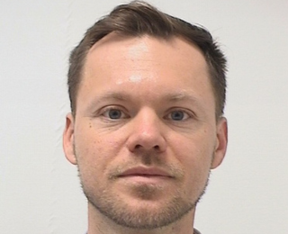 Mann i blå skjorte ser inn i kameraet