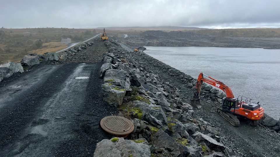 To gravemaskiner legger ut støttefylling langs dammen