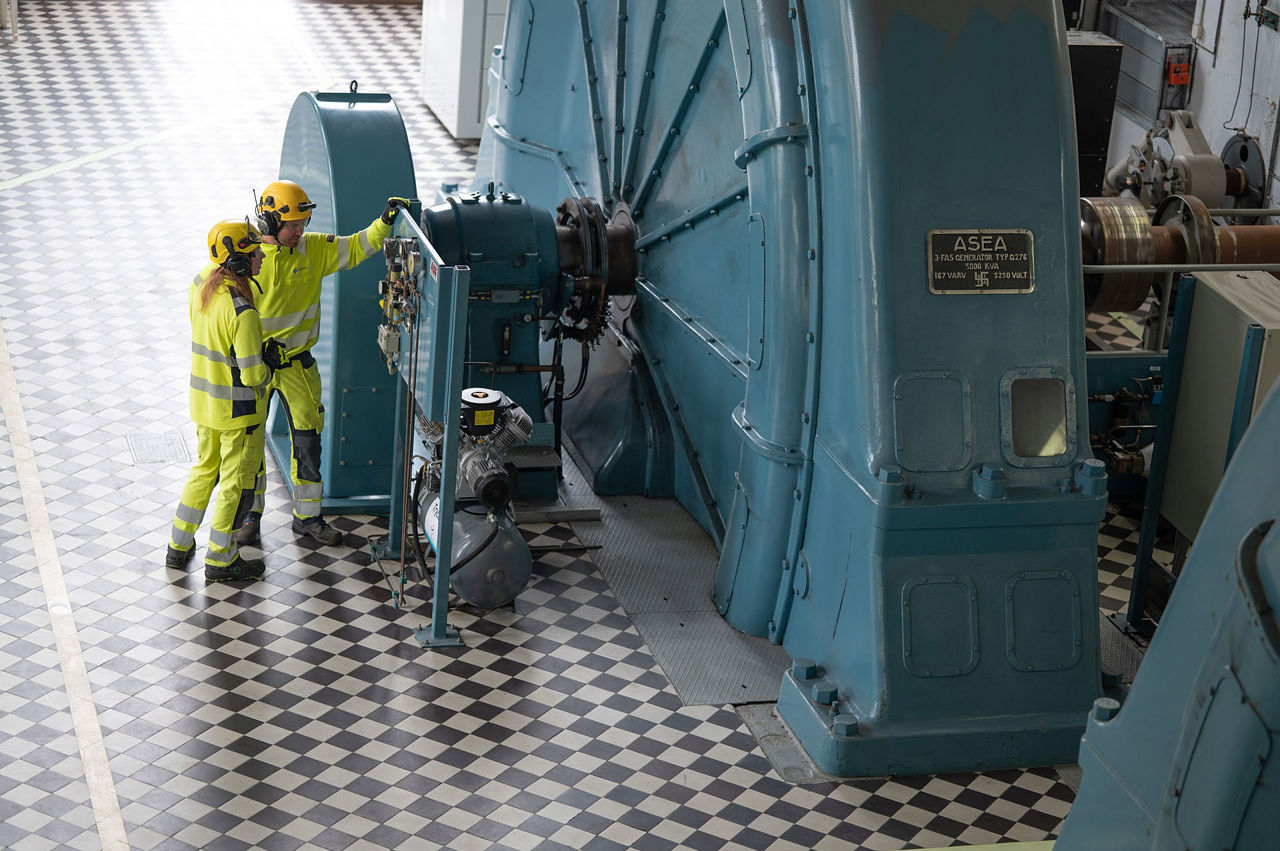To ansatte står ved siden av en turbin på innsiden av et kraftverk