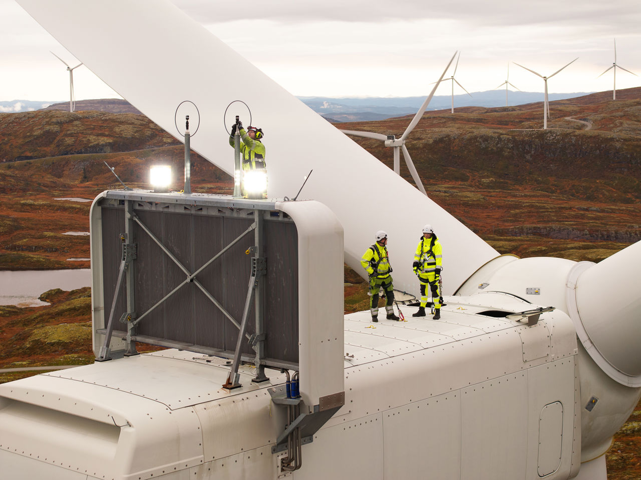 Tre ansatte jobber på toppen av en vindturbin