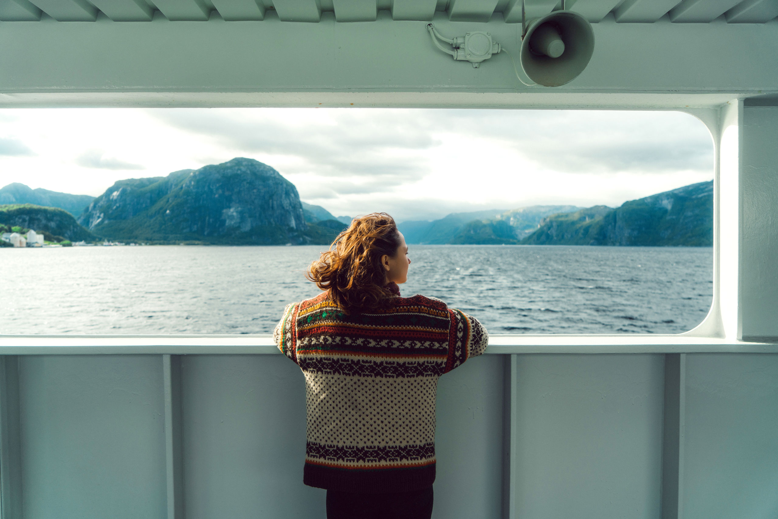 Jente står på en ferge og ser utover fjorden