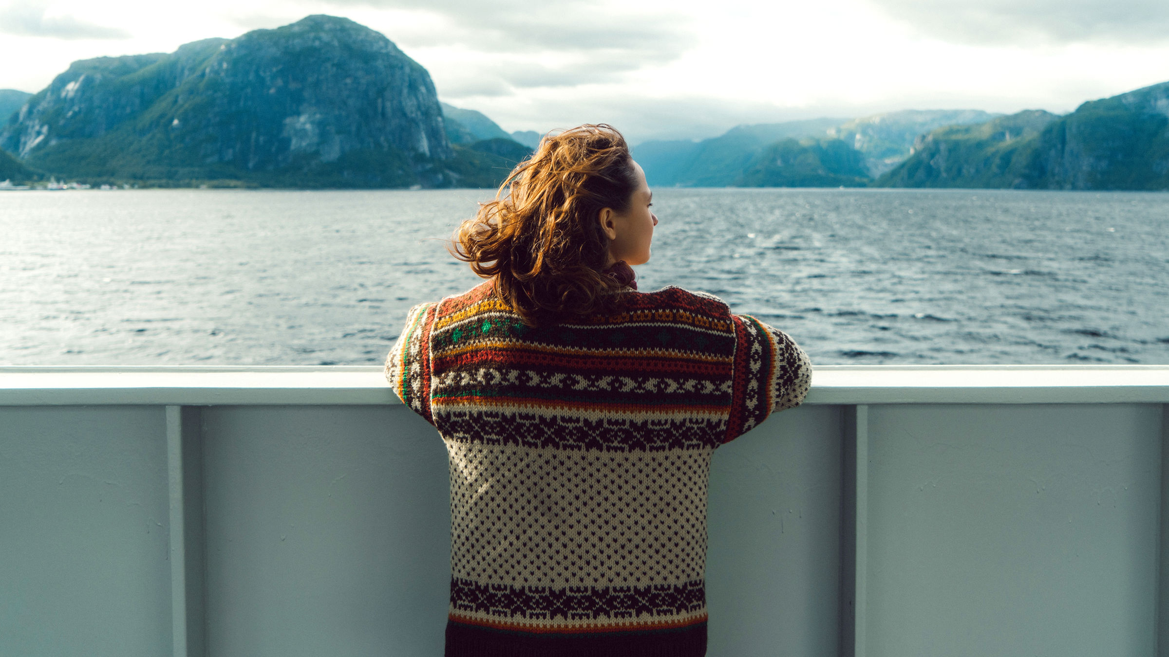 Jente står på ferge og ser utover fjord og fjell