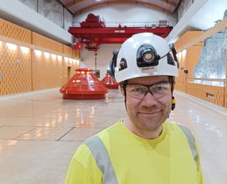 Mann med lue smiler men en bygning i bakgrunnen