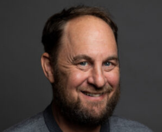 Mann med brunt hår og skjegg smiler