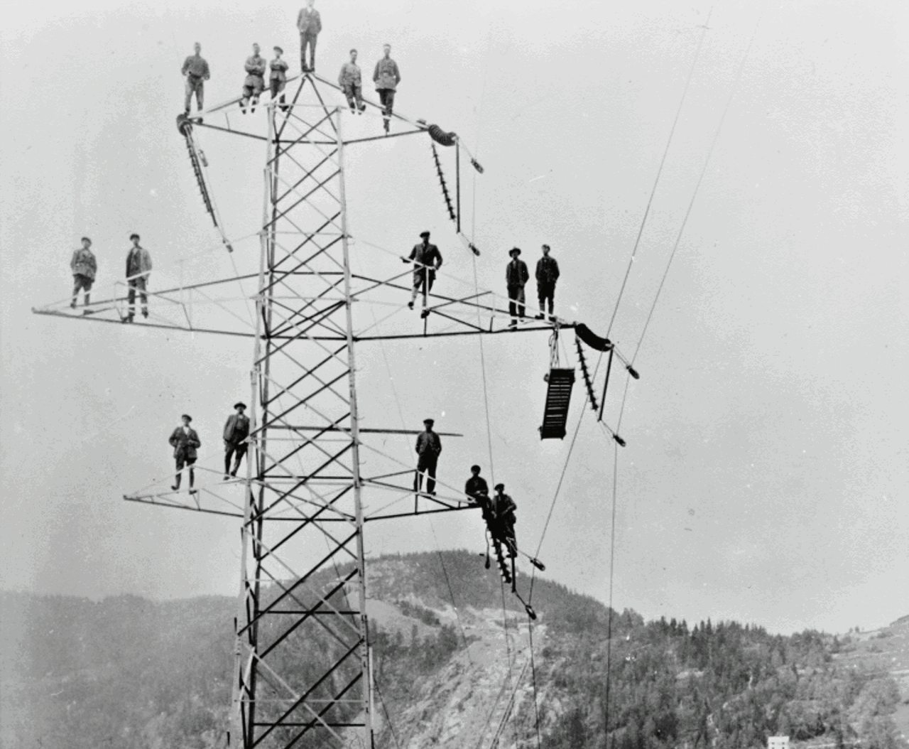 Svart-hvitt bilde av menn på en kraftmast 